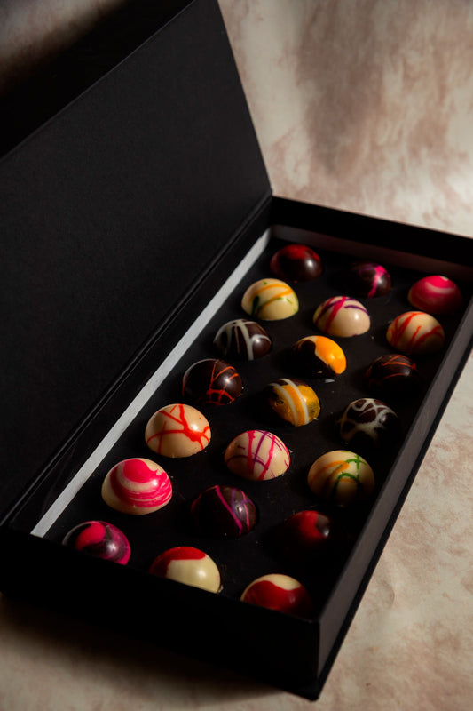 Caja negra de 21 Chocolates con Mensajes Relleno Frutal y Cacao 100% Mexicano sobre fondo de marmol para regalo empresarial