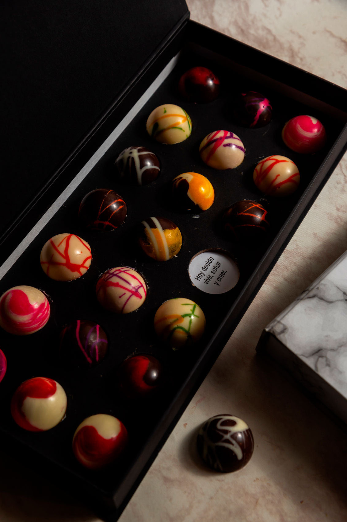 Caja negra de 21 Chocolates con Mensajes Relleno Frutal y Cacao 100% Mexicano sobre fondo de marmol para regalo empresarial