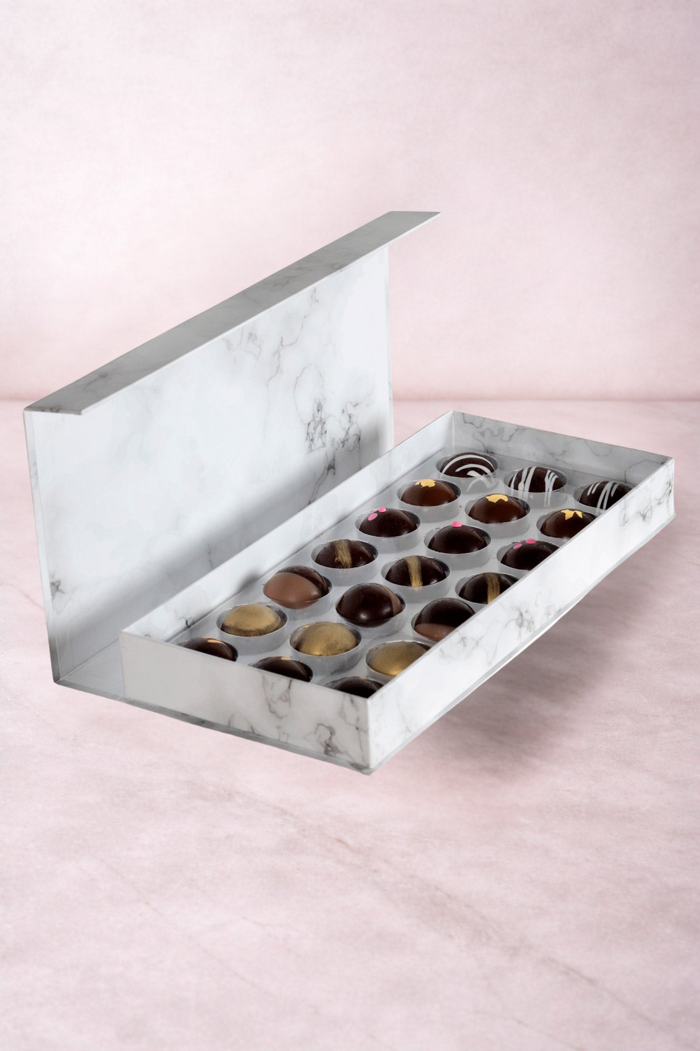 Caja blanca con chocolates negros abiertos de la marca ChocoRoux con 21 piezas rellenas y diseño premium sobre fondo mármol.