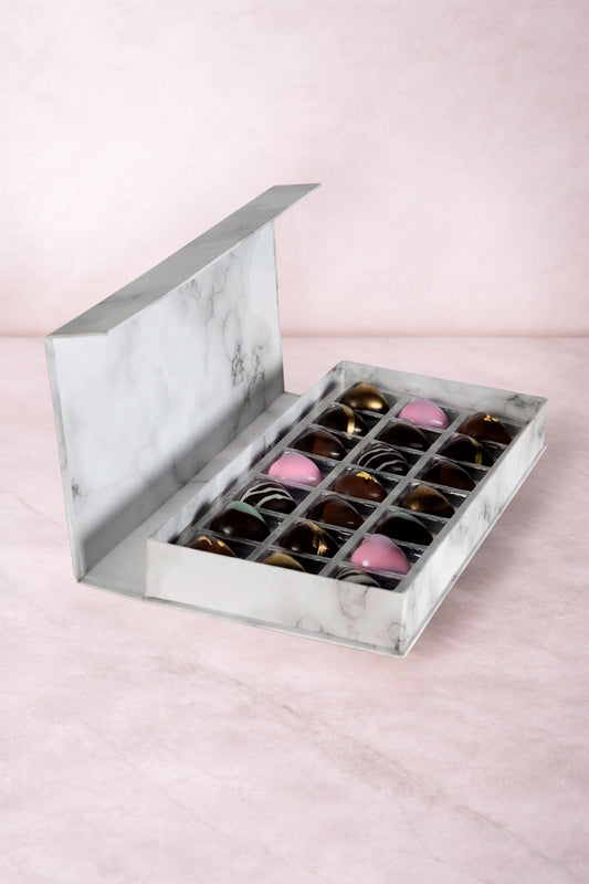 Caja blanca de chocolates negros abiertos de la marca ChocoRoux con 21 piezas rellenas y diseño premium sobre fondo mármol.
