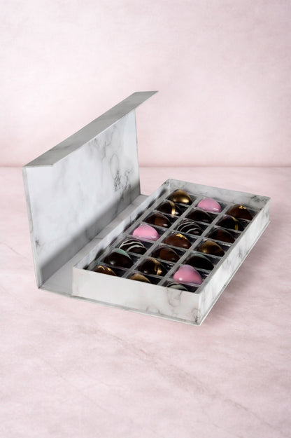 Caja blanca de chocolates negros abiertos de la marca ChocoRoux con 21 piezas rellenas y diseño premium sobre fondo mármol.